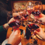 Close up shot of group of people clinking glasses with wine or champagne in front of bokeh background. older people hands.